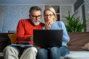 An older couple sitting together, focused on a laptop screen.