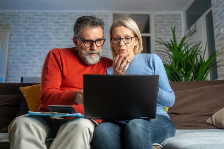An older couple sitting together, focused on a laptop screen.