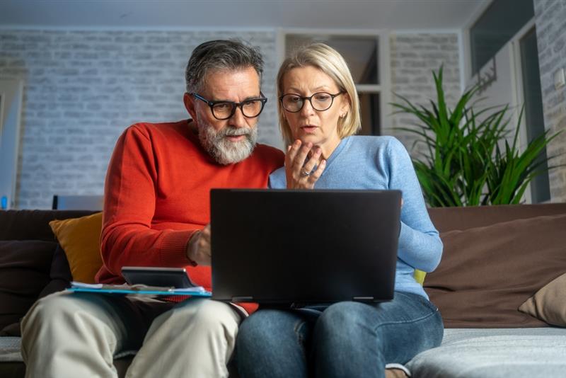 An older couple sitting together, focused on a laptop screen.