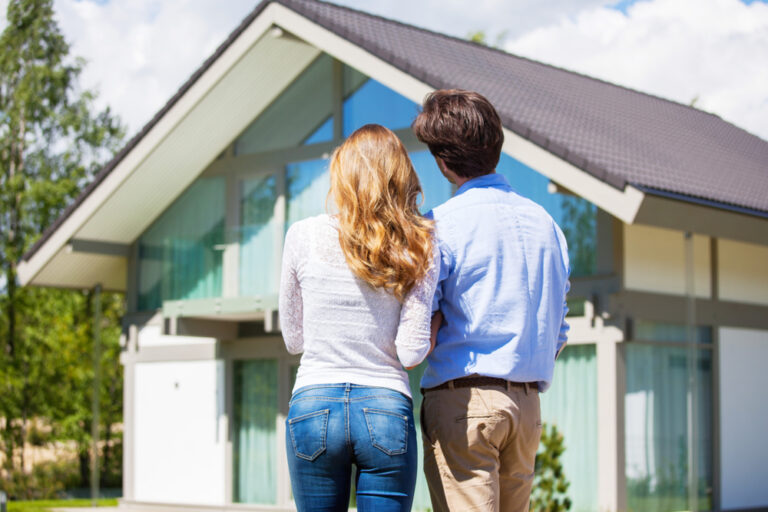 A couple stands together in front of a house