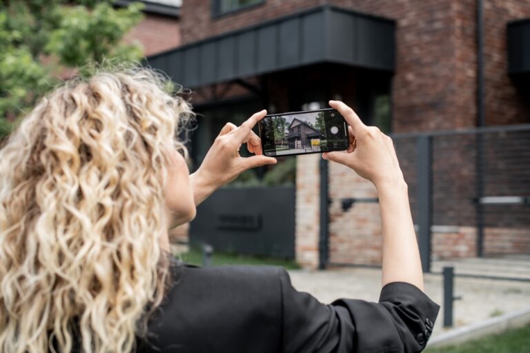 A woman photographing a house with her smartphone.