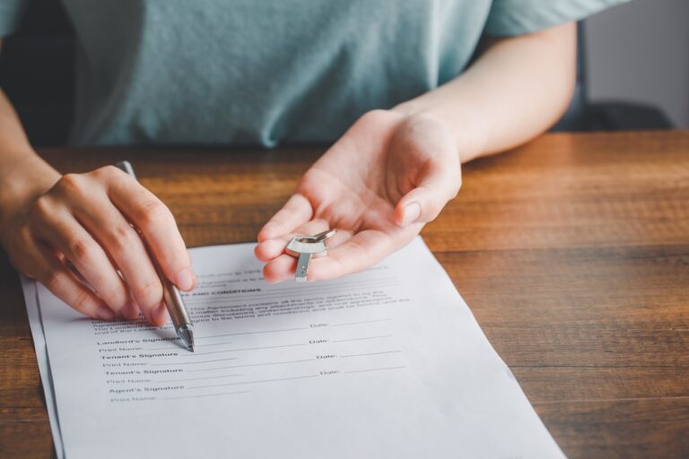 Woman signing a contract with a pen, holding keys in her other hand.
