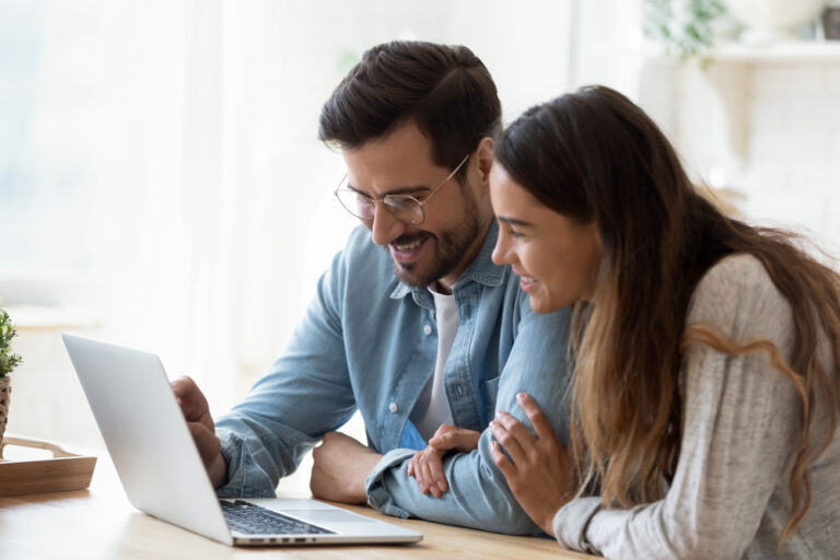 A man and woman are focused on a laptop, discussing ideas for a blog post together.