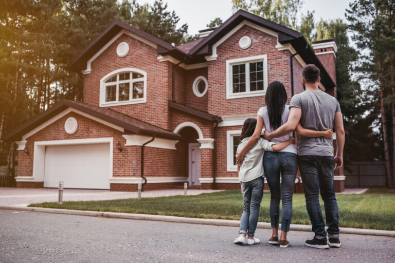 A family poses together in front of their house, smiling happily.