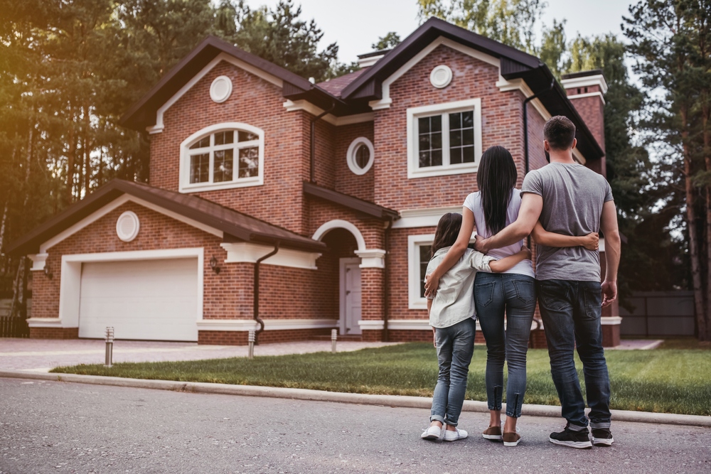 A family poses together in front of their house, smiling happily.