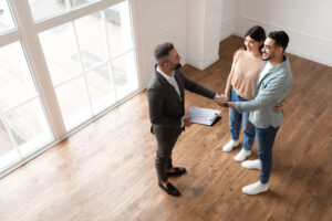 Man and woman shaking hands with an estate agent in a vacant room.