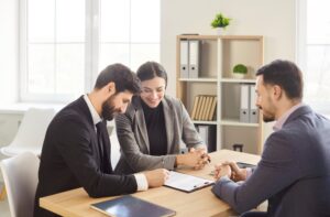 Three business people at a table, with one signing a document for an estate agreement.