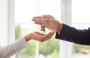 A man hands a key to a woman, symbolizing homeownership transfer.