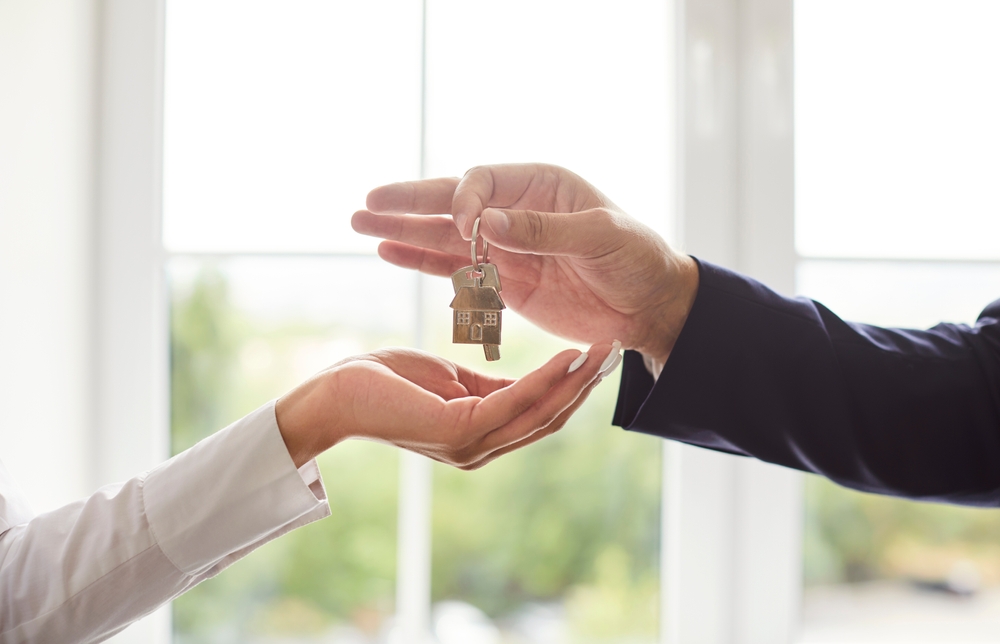 A man hands a key to a woman, symbolizing homeownership transfer.