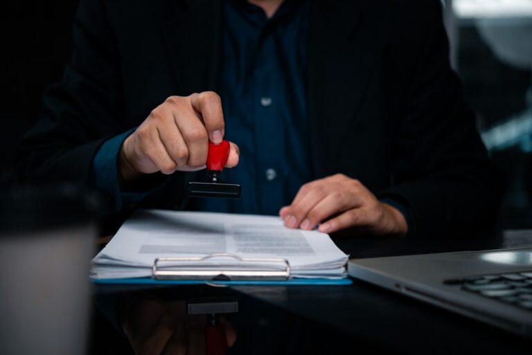 A person in a suit holding a red rubber stamp, ready to stamp a document.