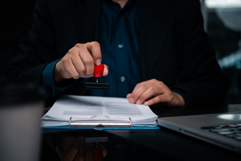 A person in a suit holding a red rubber stamp, ready to stamp a document.