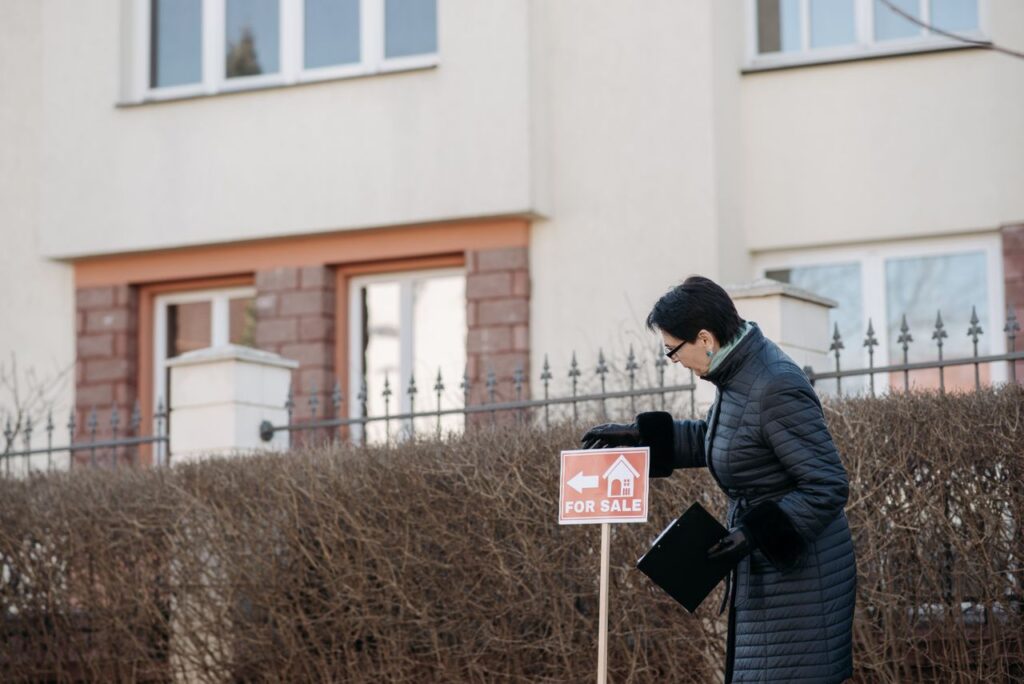 A woman stands in front of a house, holding a sign.