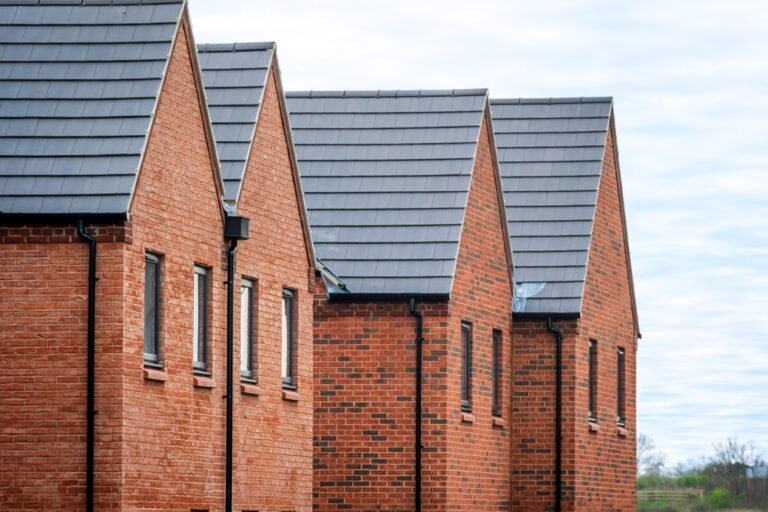 A series of red brick homes topped with black roofs in a row.